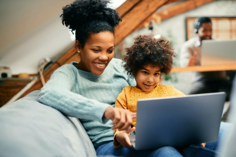 Happy black mother and daughter surfing the net on laptop at home.