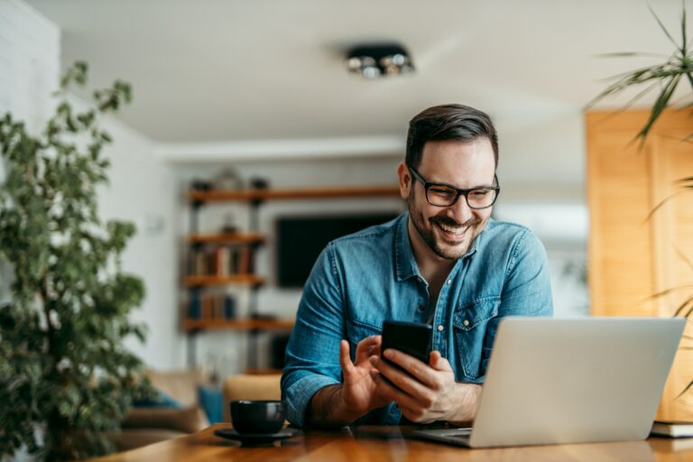 Portrait of a happy man with smart phone and laptop, indoors.